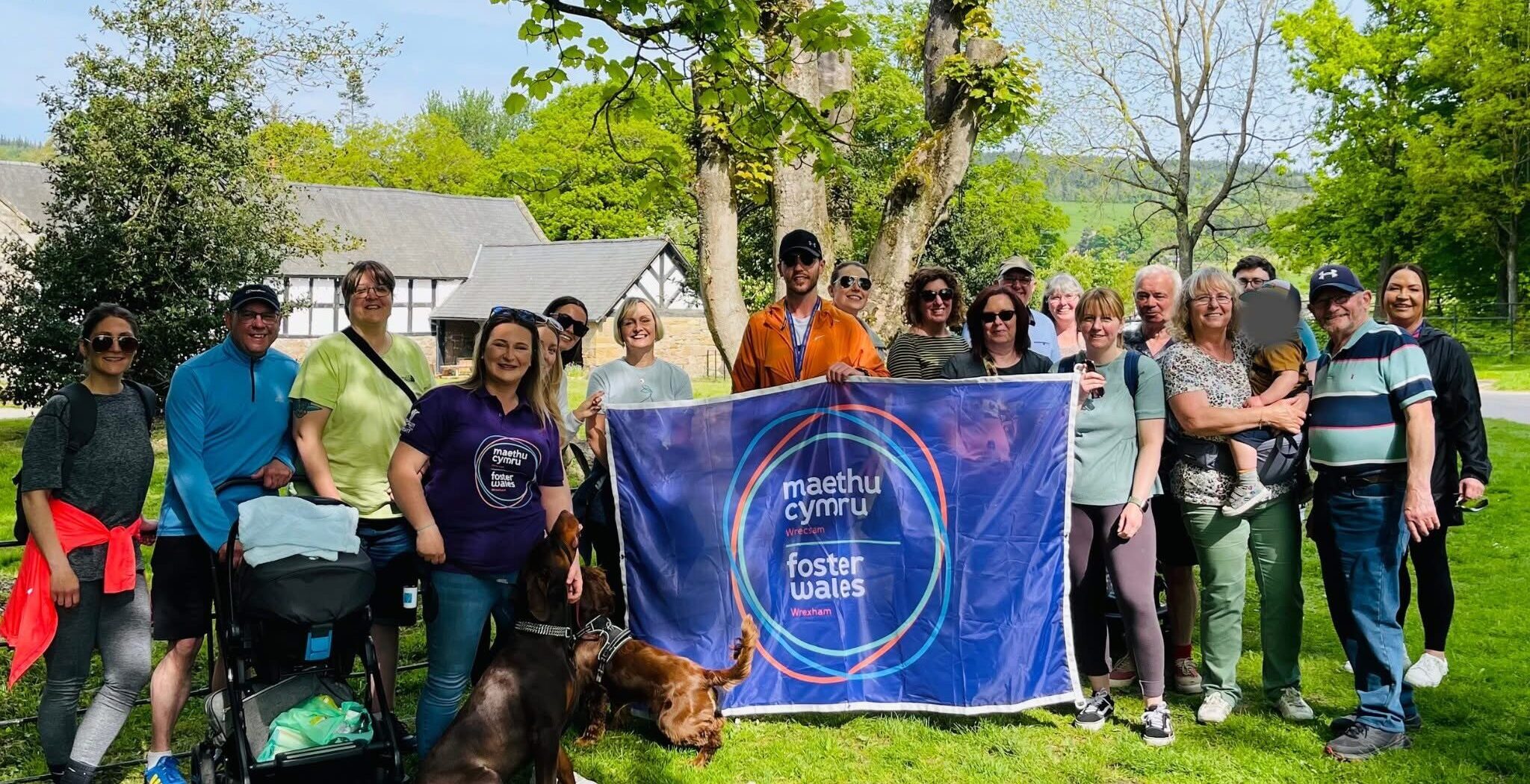 A group of Foster Carers and team members outside holding a Foster Wales banner