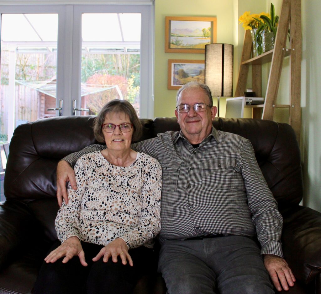 Foster carers Trish and Keving smilling on the sofa 